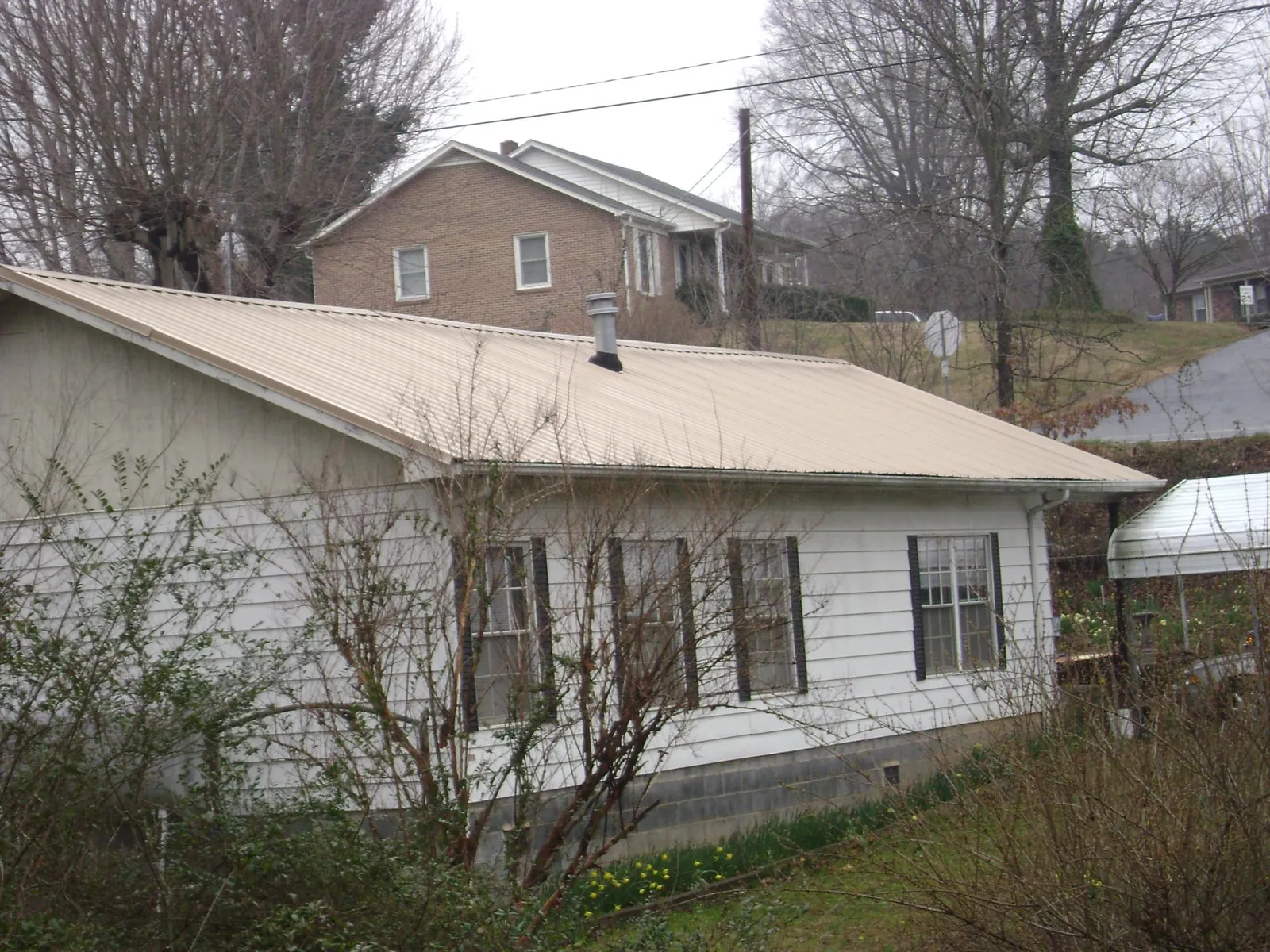 Tan metal roof on a white sided house set into a hillside — Commercial Roofing by Roofing Brothers in Sardis
