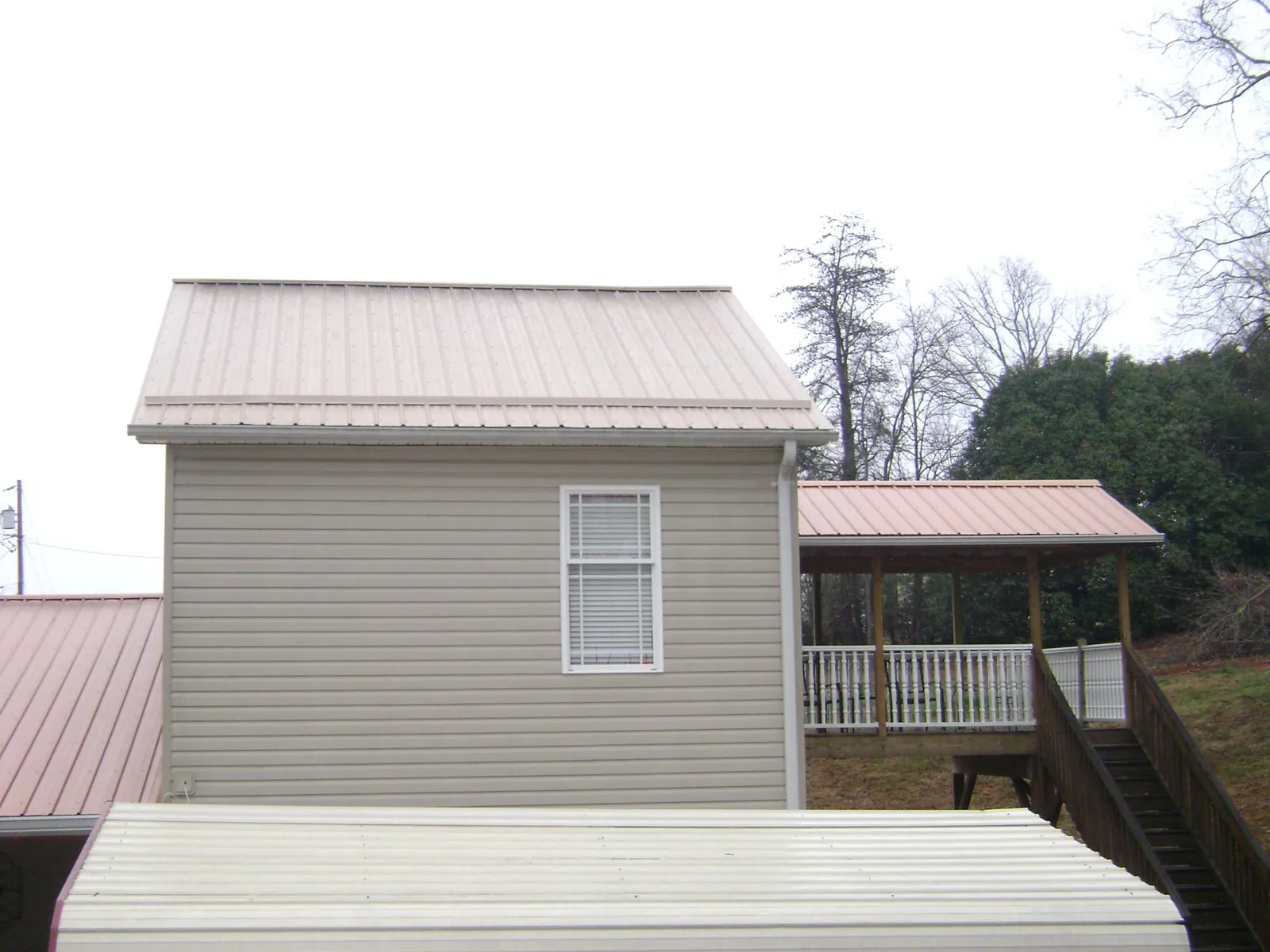 Tan metal roofs on a two story addition and attached porch, from a Roof Replacement job in Sardis